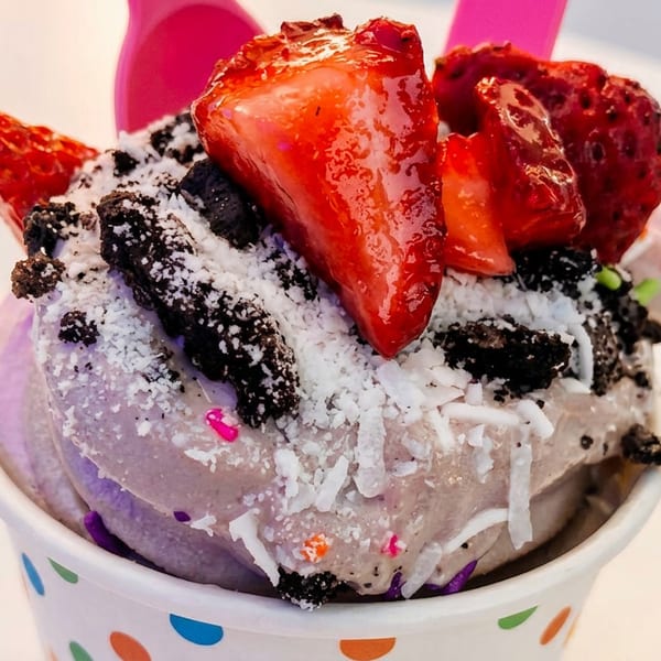Purple frozen yogurt topped with fresh strawberries, crushed cookies, shredded coconut, and sprinkles.