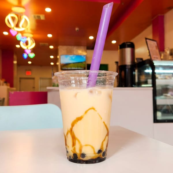 Bubble tea with caramel drizzle and a purple straw on a table in a colorful restaurant.
