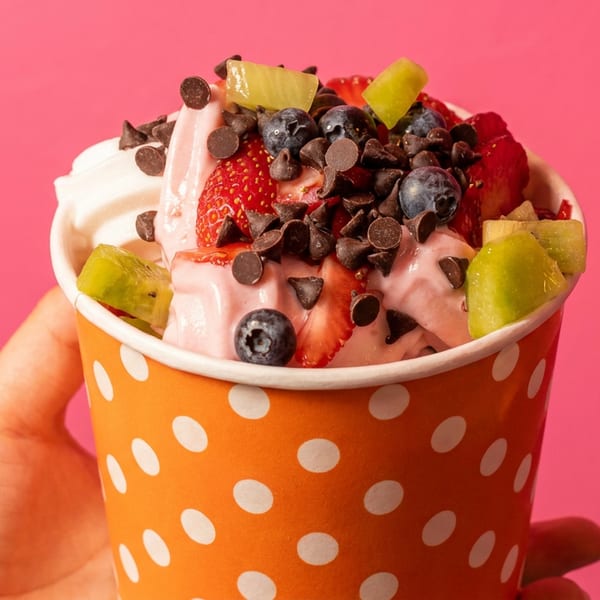 Hand holding a polka-dotted cup of frozen yogurt with fruit and chocolate chips.