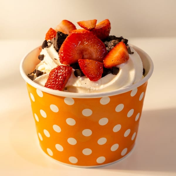 Orange polka-dot cup filled with frozen yogurt, topped with fresh strawberries and chocolate chips.